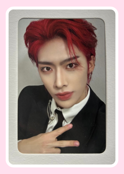 ZB1 Ricky with red hair wearing a black suit and white shirt, making a peace sign.